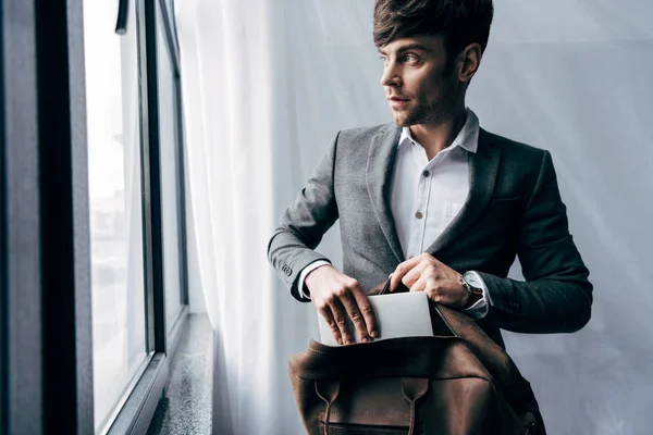 Selective focus of businessman in jacket putting laptop in bag at office — Stock Photo