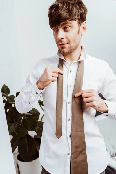 Happy businessman in white shirt tying neck tie at home — Stock Photo