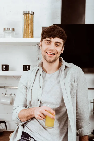 Happy young man drinking orange juice in kitchen at home — Stock Photo