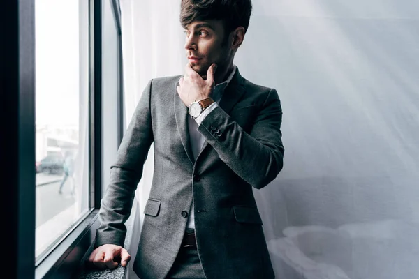 Вдумливий молодий бізнесмен в куртці, дивлячись в офіс — стокове фото