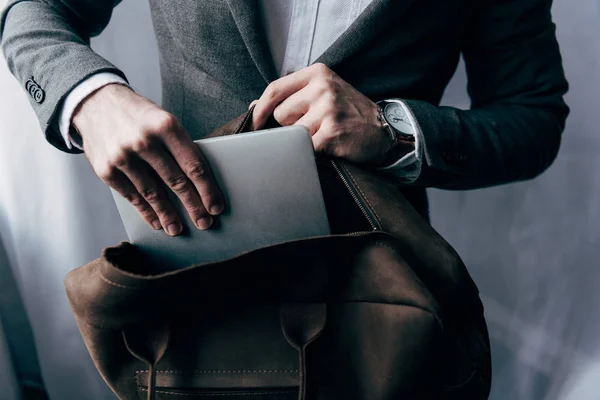 Cropped image of businessman in jacket putting laptop in bag — Stock Photo