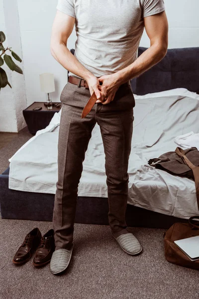 Imagen recortada de hombre de negocios poniéndose cinturón en el dormitorio en casa - foto de stock