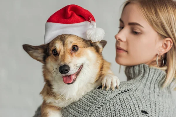 Close-up portrait of young woman carrying adorable corgi dog in santa hat — Stock Photo