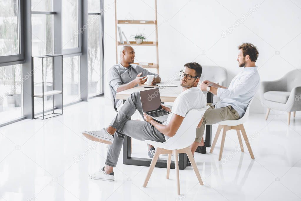 multicultural group of businessmen sitting at workplace in light modern office
