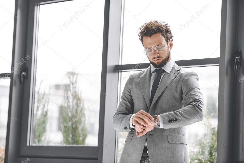 portrait of handsome businessman in eyeglasses looking at watch to check time