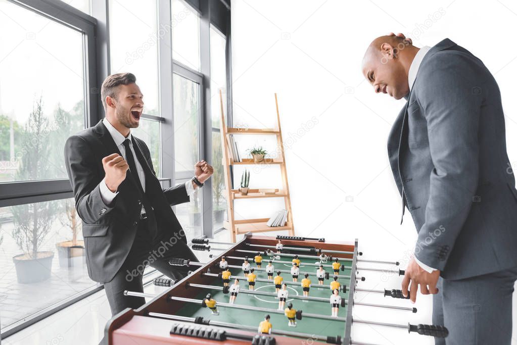 excited businessman playing table football with coworker in office