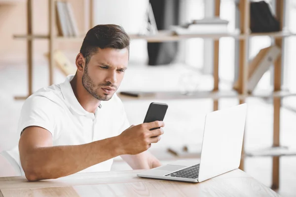 Retrato de empresário focado usando smartphone no local de trabalho com laptop no escritório — Fotografia de Stock