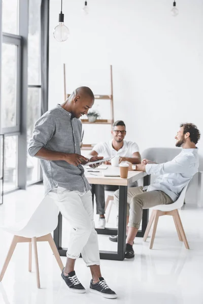 Afrikanisch-amerikanischer Mann nutzt Tablet, während Kollegen am Arbeitsplatz im Büro über Strategie diskutieren — Stockfoto