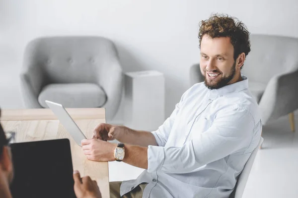 Retrato de un hombre de negocios sonriente usando una tableta mientras conversaba con un colega en la oficina - foto de stock