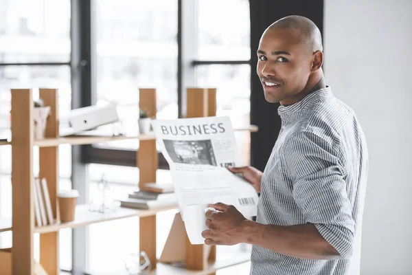 Vista lateral do empresário afro-americano com jornal e xícara de café no escritório — Fotografia de Stock
