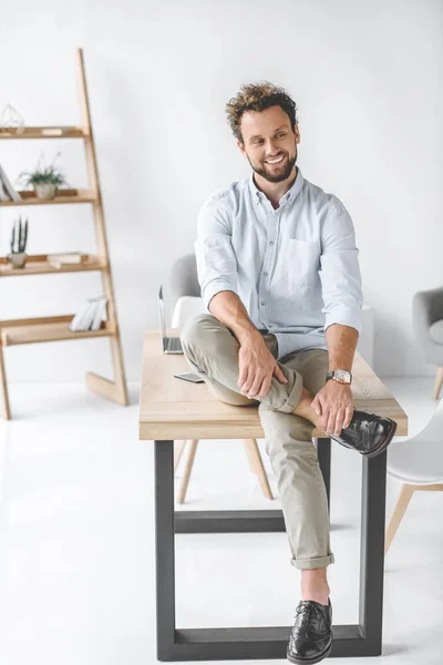 Jovem homem de negócios sorridente sentado na mesa no escritório moderno — Fotografia de Stock