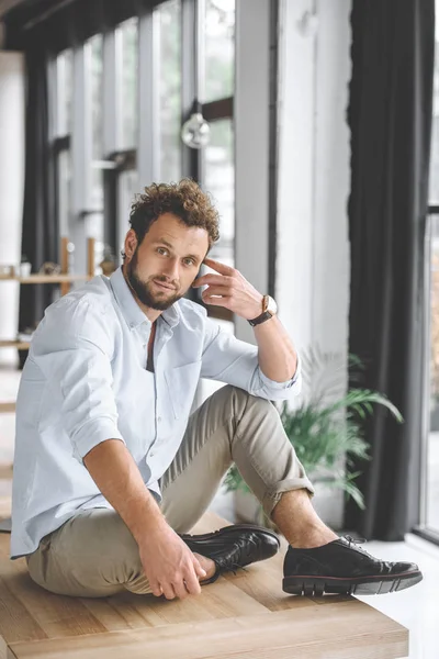 Thoughtful young businessman sitting on table in modern office — Stock Photo