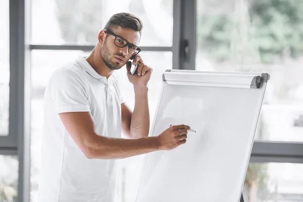 Hombre de negocios hablando en el teléfono inteligente mientras que hace la presentación en la pizarra blanca en la oficina - foto de stock