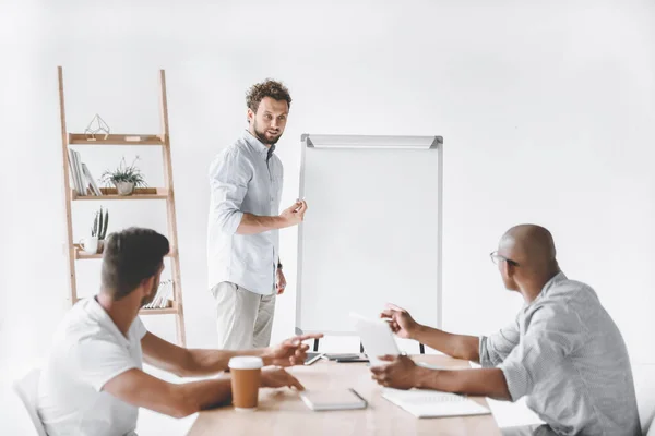 Joven hombre de negocios en la pizarra blanca haciendo presentación a los colegas - foto de stock