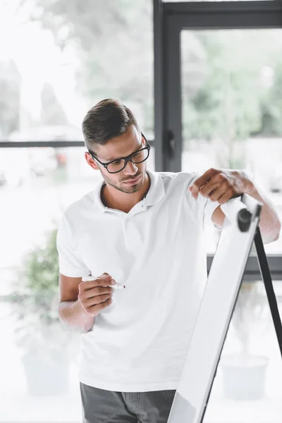 Young focused businessman making presentation at white board in office — Stock Photo