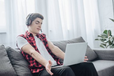 kanepede otururken dizüstü bilgisayarda oyun oynama kulaklık ile genç çocuk 