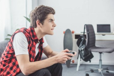 teen boy playing video game with gamepad at home clipart