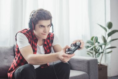 teenager with headset playing video game with gamepad at home clipart