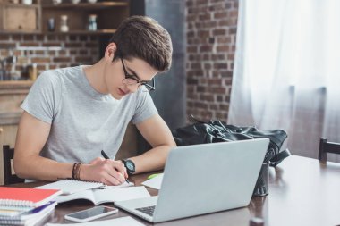 ciddi öğrenci ödev masada dizüstü ve smartphone ile yazma