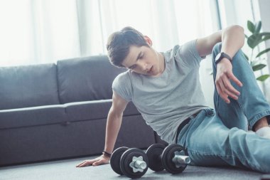 dumbbells ile eğitimden sonra katta oturan genç yorgun çocuk  