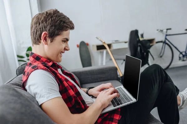 Sorrindo Adolescente Digitando Laptop Enquanto Sentado Sofá — Fotografia de Stock