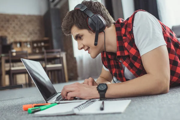 Uśmiechający Się Teen Chłopiec Słuchawkami Gry Laptopa Leżąc Podłodze Rezerwowym — Zdjęcie stockowe