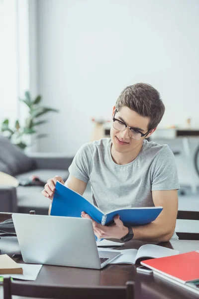 コピーブックとノート パソコンを自宅で宿題をしている男子生徒 — ストック写真