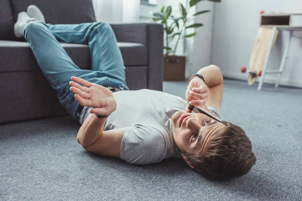 Adolescente Com Gesto Encolher Ombros Falando Smartphone Enquanto Deitado Chão — Fotografia de Stock