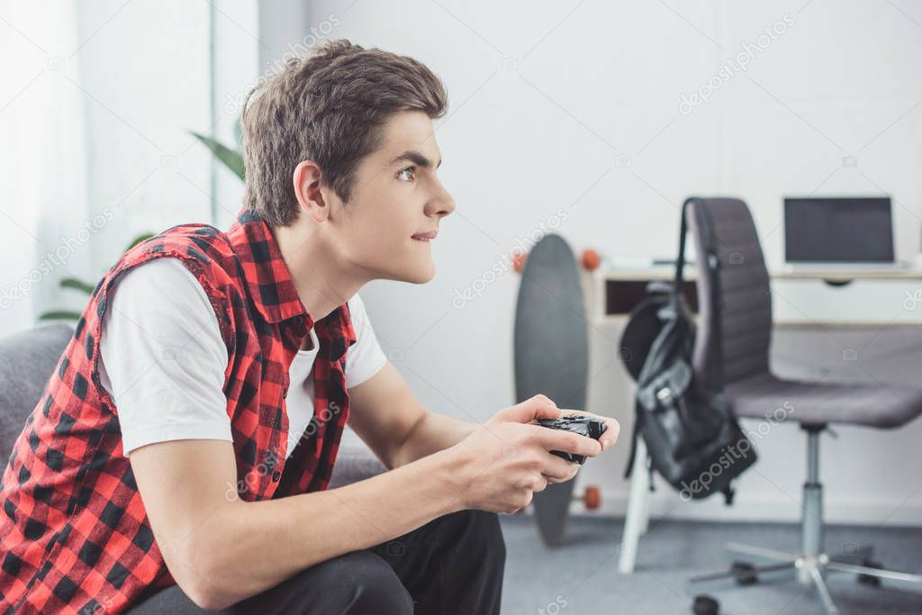 teen boy playing video game with gamepad at home