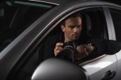 Paparazzi blicken auf Armbanduhr und spionieren mit Objektiv aus seinem Auto 