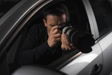 Erkek paparazzi gözetim fotoğraf makinesi ile arabasından yapıyor. 