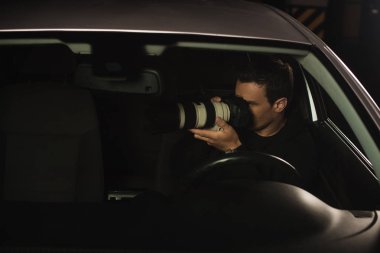 paparazzi doing surveillance by camera from his car  clipart