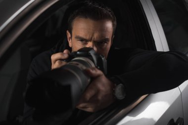 concentrated paparazzi spying by camera with object glass from his car  clipart