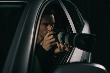 focused paparazzi doing surveillance by camera from his car  clipart