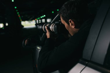 rear view of male paparazzi spying by camera with object glass from his car  clipart