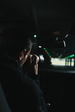 rear view of man doing surveillance by camera with object glass from his car clipart