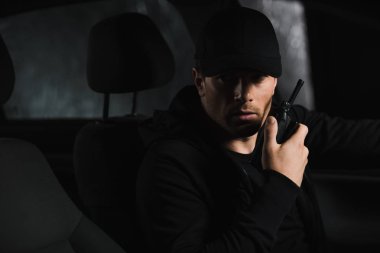 ciddi erkek özel dedektif gözetleme yapıyor ve arabasında walkie talkie kullanarak şapkalı