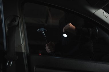 cropped shot of male robber with flashlight and hammer preparing to intrude car  clipart
