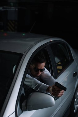 Araba silahtan tarafından hedefleyen güneş gözlüklü erkek gizli ajanın yüksek açılı görünüş