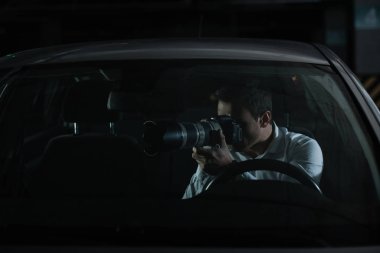 male private detective spying by camera with object glass from his car clipart