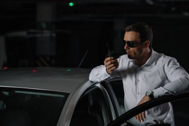 Erkek gizli ajan car yakınındaki walkie talkie kullanarak güneş gözlüğü 