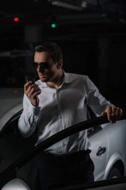 ciddi erkek gizli ajan car yakınındaki walkie talkie kullanarak güneş gözlüğü 
