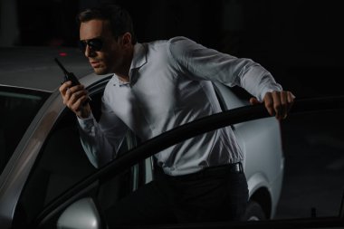 Erkek gizli ajan car yakınındaki walkie talkie kullanarak güneş gözlüğü 
