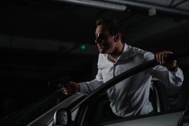 Erkek gizli ajan silahla arabada oturarak güneş gözlüğü