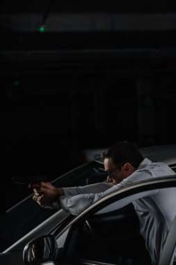 Erkek ajanı arabanın yakınında duran ve silah tarafından hedefleyen güneş gözlüğü 