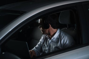 Erkek özel dedektif gözetim araba içinde laptop ile yapıyor Kulaklığımda yan görünüm
