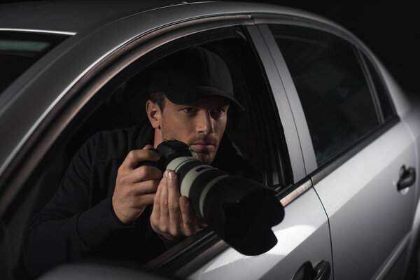male paparazzi in cap spying with camera from his car 
