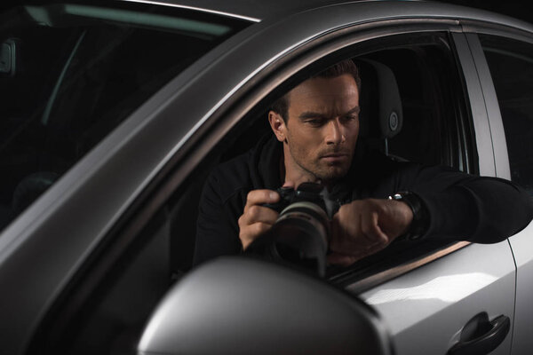 male paparazzi looking at wristwatch and spying by camera with lens from his car 