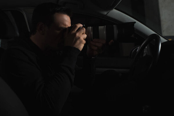 side view of concentrated man doing surveillance by camera with object glass from his car 