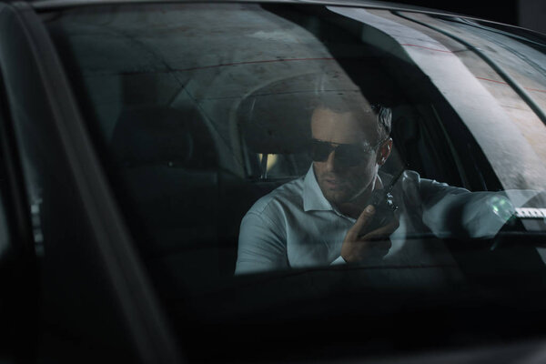 male undercover agent using talkie walkie and spying from car